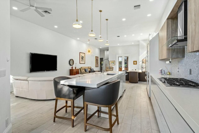 kitchen with wall chimney exhaust hood, a kitchen bar, sink, decorative light fixtures, and an island with sink