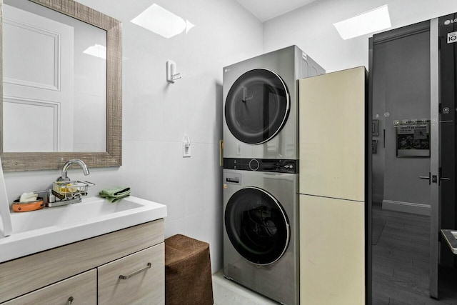 washroom with stacked washing maching and dryer, sink, tile walls, and light wood-type flooring