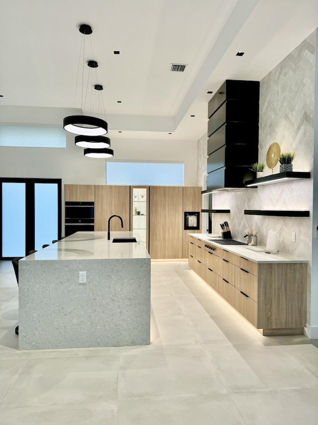 kitchen with a large island, sink, hanging light fixtures, backsplash, and light stone counters