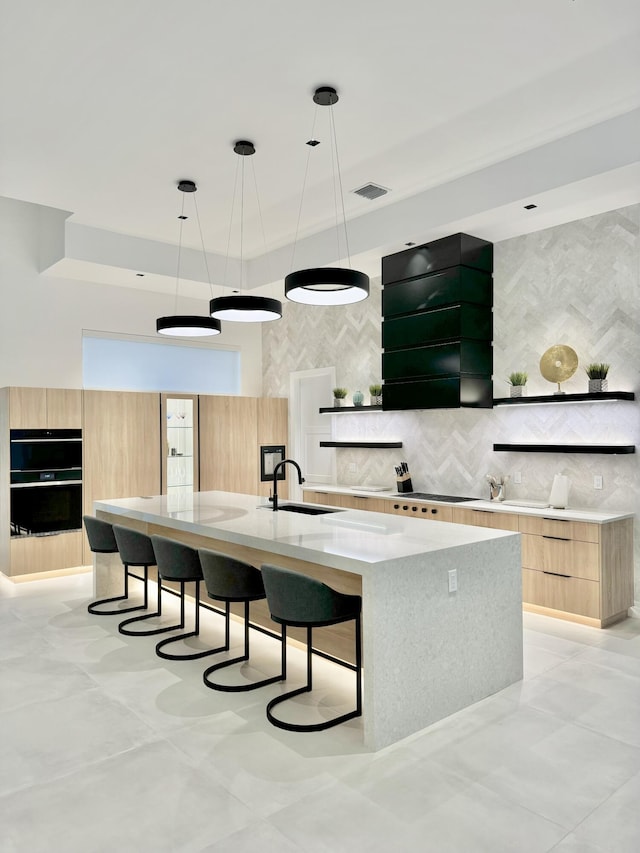 kitchen featuring pendant lighting, light brown cabinetry, double oven, sink, and a spacious island