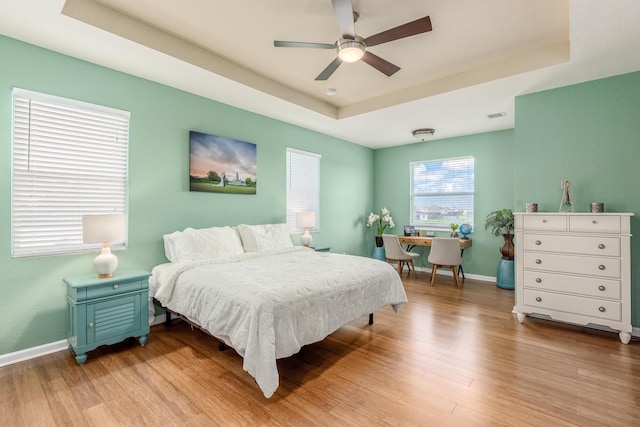 bedroom with a raised ceiling, ceiling fan, and light hardwood / wood-style flooring