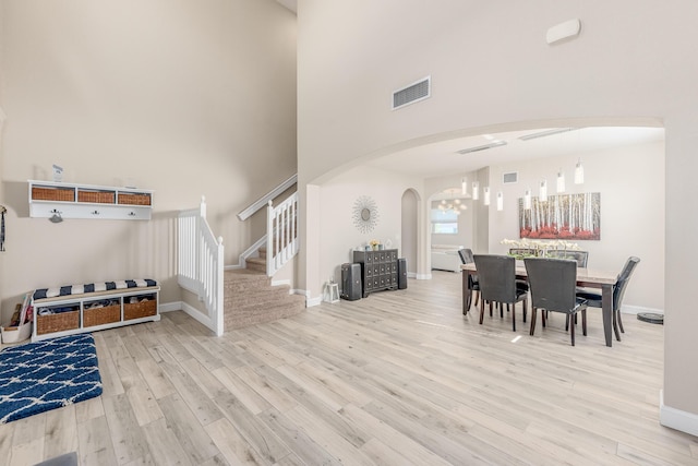 dining room featuring a towering ceiling, a notable chandelier, and light wood-type flooring