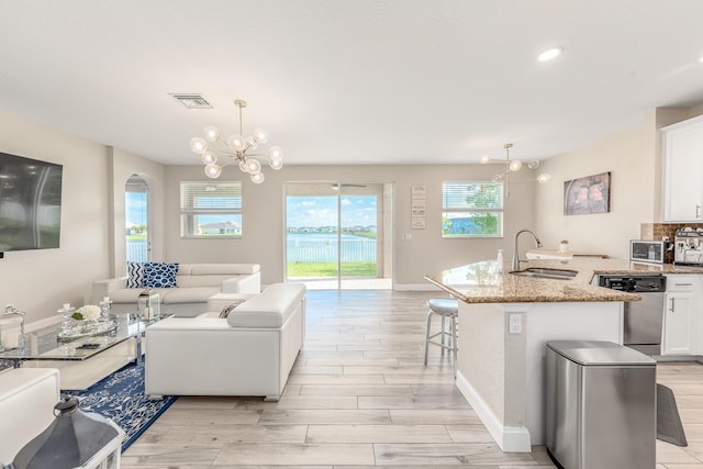 kitchen featuring sink, dishwasher, white cabinetry, a center island with sink, and decorative light fixtures