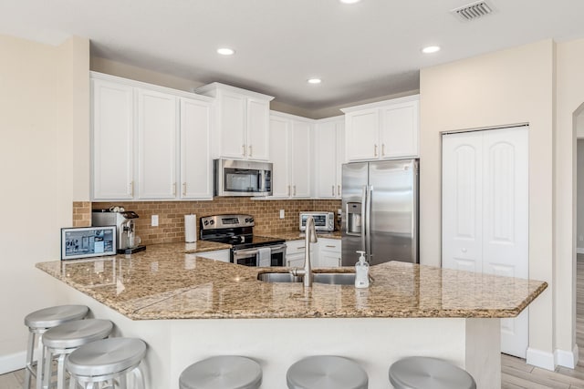 kitchen with appliances with stainless steel finishes, a breakfast bar area, white cabinets, and kitchen peninsula