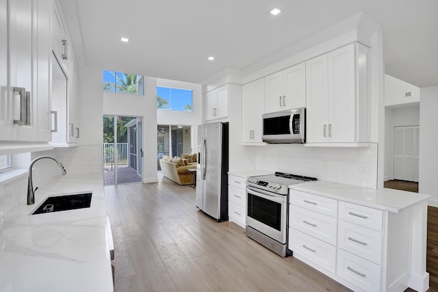 kitchen with sink, appliances with stainless steel finishes, white cabinetry, light stone countertops, and light hardwood / wood-style floors