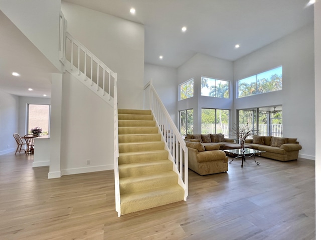 staircase featuring a towering ceiling, wood-type flooring, and plenty of natural light