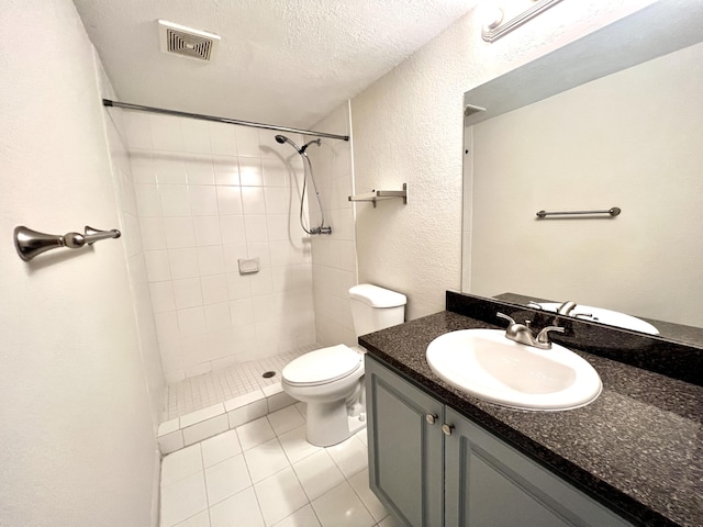 bathroom featuring tile patterned floors, toilet, a textured ceiling, a tile shower, and vanity