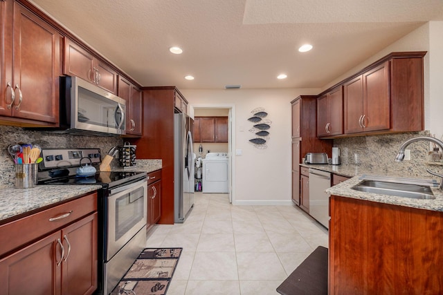 kitchen with sink, light stone counters, light tile patterned floors, appliances with stainless steel finishes, and independent washer and dryer