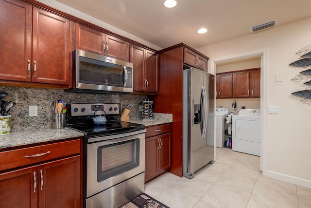 kitchen featuring appliances with stainless steel finishes, backsplash, washing machine and dryer, light stone counters, and light tile patterned flooring