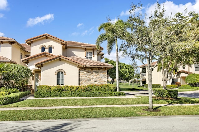 mediterranean / spanish home with stone siding, stucco siding, a tile roof, and a front yard