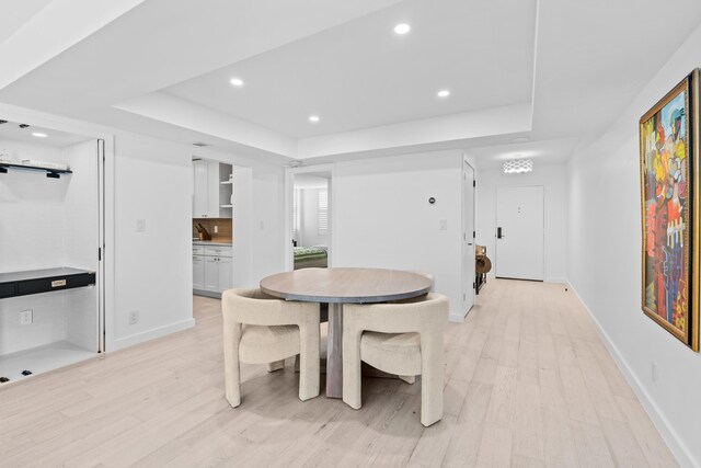 dining space with a tray ceiling and light wood-type flooring