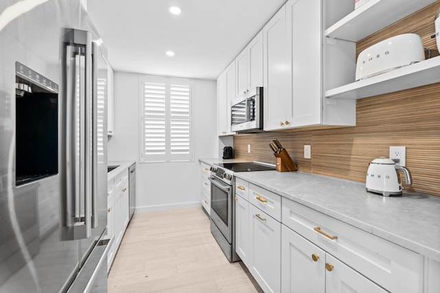 kitchen with appliances with stainless steel finishes, light stone countertops, light wood-type flooring, and white cabinets