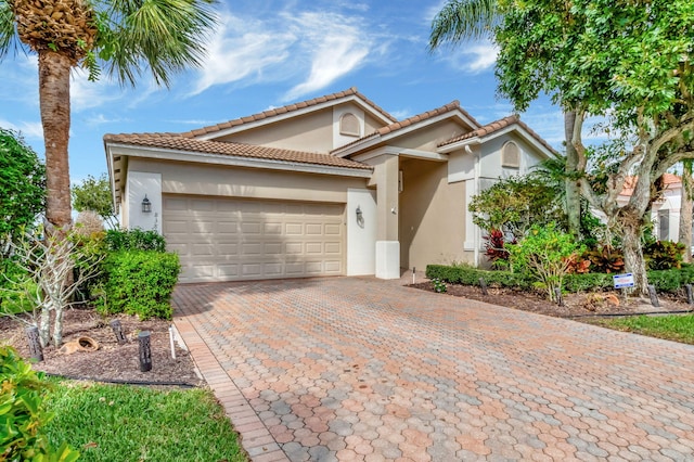 mediterranean / spanish-style house featuring an attached garage, a tile roof, decorative driveway, and stucco siding