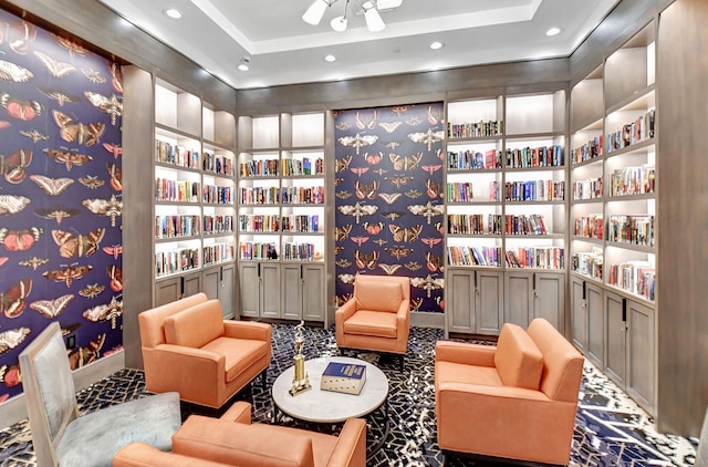 living area with a tray ceiling, bookshelves, wallpapered walls, and recessed lighting