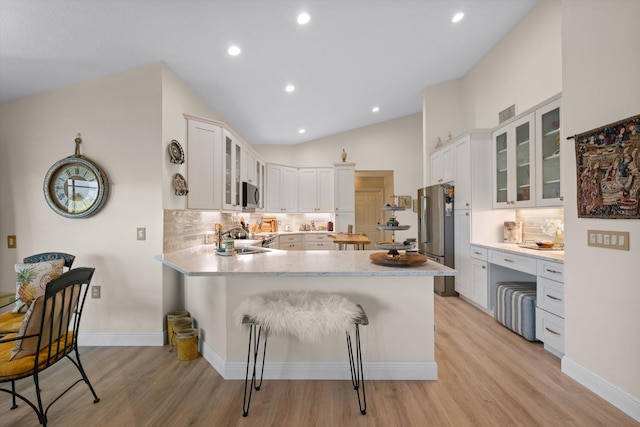 kitchen featuring lofted ceiling, a breakfast bar, appliances with stainless steel finishes, white cabinets, and kitchen peninsula