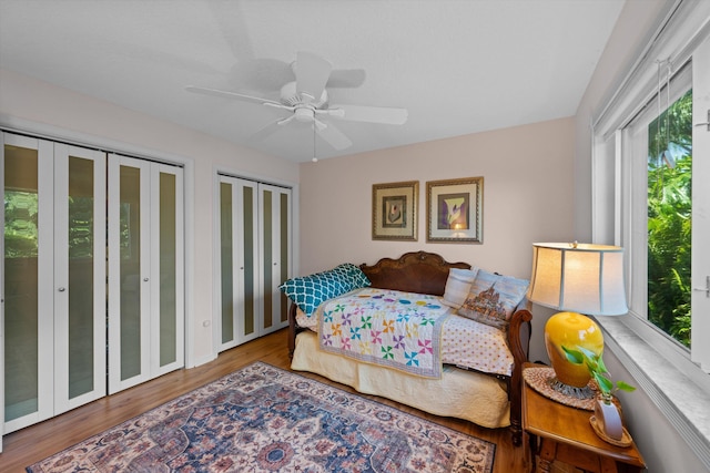 bedroom featuring hardwood / wood-style flooring, ceiling fan, and multiple closets