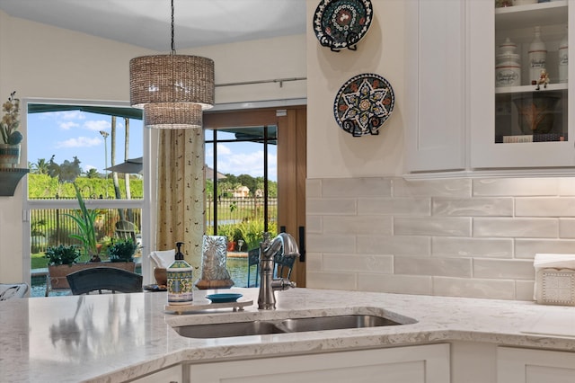 kitchen featuring sink, hanging light fixtures, tasteful backsplash, light stone countertops, and white cabinets