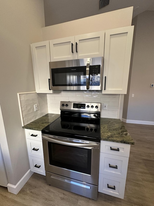 kitchen with dark wood-type flooring, appliances with stainless steel finishes, dark stone countertops, tasteful backsplash, and white cabinets