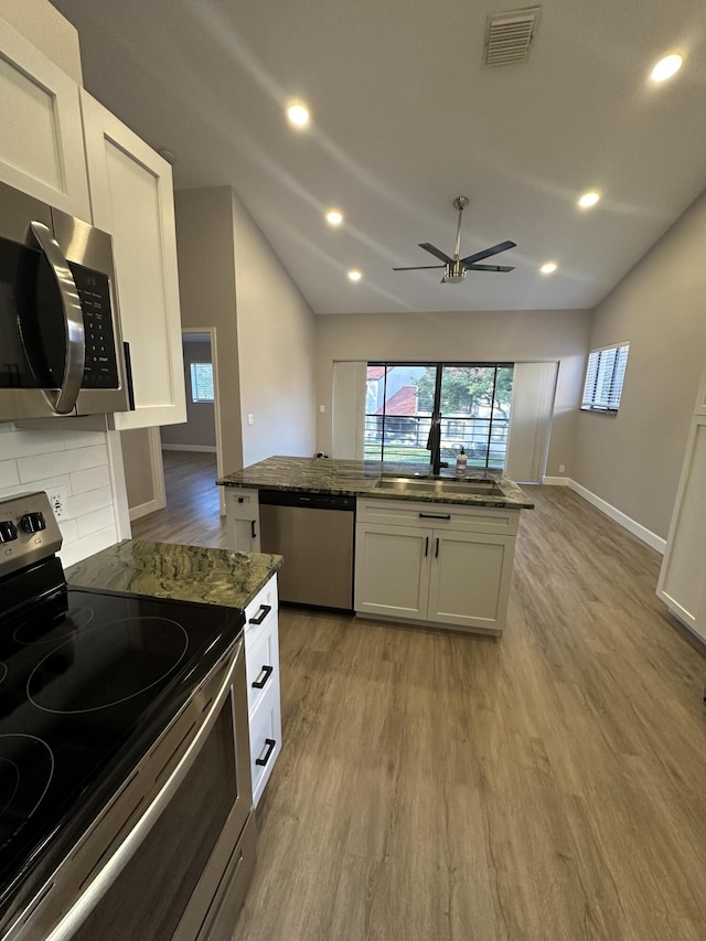 kitchen featuring lofted ceiling, sink, appliances with stainless steel finishes, dark stone countertops, and white cabinets