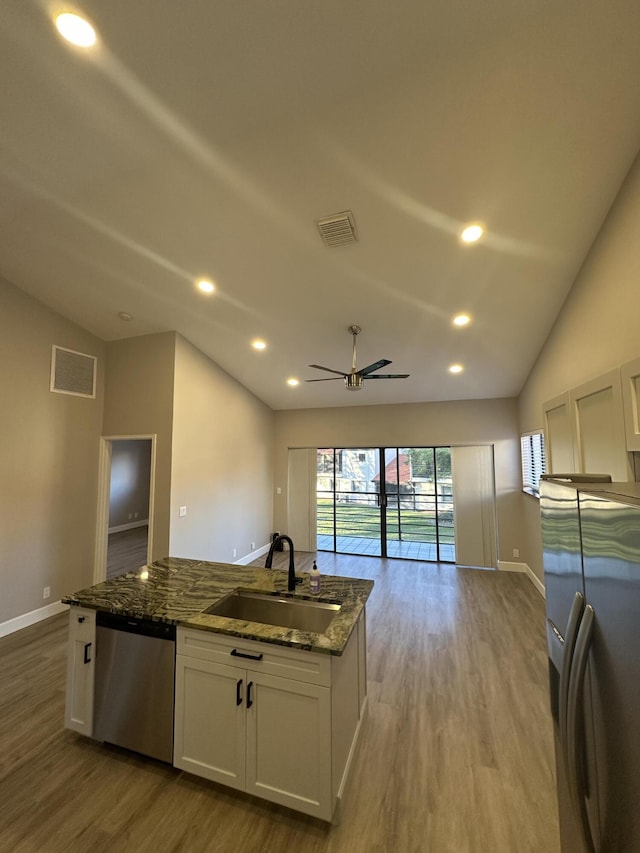 kitchen with vaulted ceiling, white cabinetry, sink, dark stone countertops, and stainless steel appliances