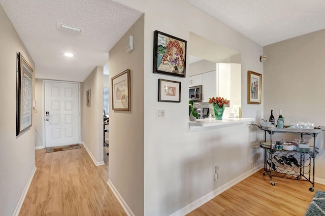 corridor with a textured ceiling, baseboards, and light wood-style floors