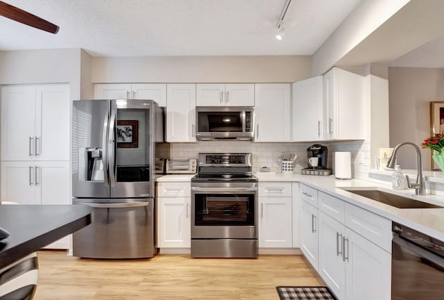 kitchen featuring stainless steel appliances, light countertops, white cabinets, and a sink