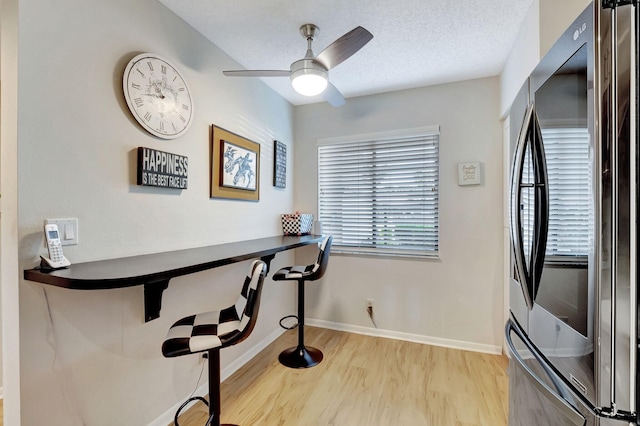 dining area with a textured ceiling, ceiling fan, light wood-type flooring, and baseboards