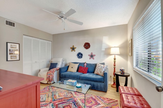 living room with light wood-type flooring, a ceiling fan, visible vents, and a textured ceiling