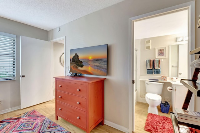 bedroom with light wood finished floors, visible vents, a textured ceiling, ensuite bath, and baseboards