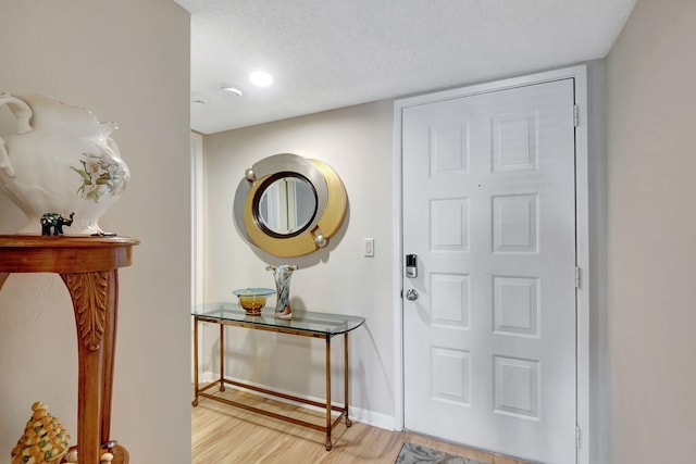 entryway with light wood finished floors, baseboards, and a textured ceiling