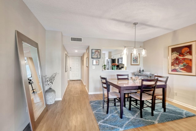 dining space featuring visible vents, a textured ceiling, baseboards, and wood finished floors