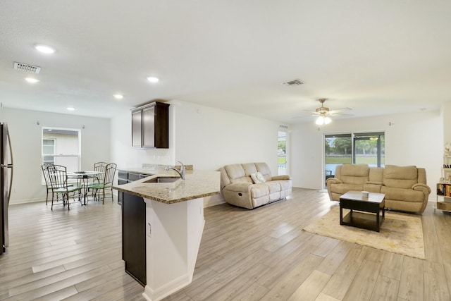 kitchen featuring a peninsula, light stone counters, visible vents, and light wood-style floors