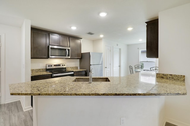 kitchen featuring a peninsula, light stone countertops, stainless steel appliances, and a sink