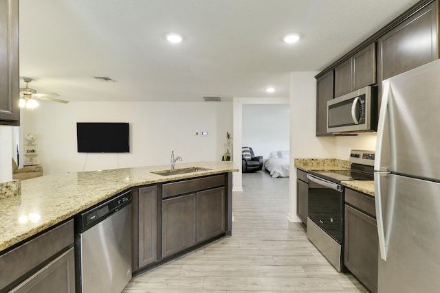 kitchen featuring light stone counters, stainless steel appliances, visible vents, open floor plan, and a sink