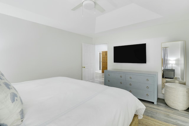 bedroom featuring ceiling fan, a raised ceiling, and light hardwood / wood-style flooring