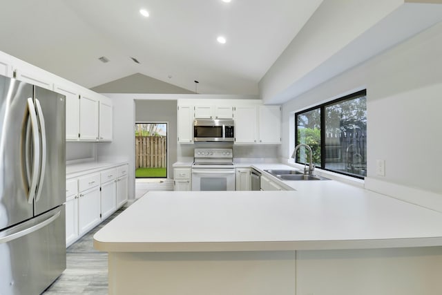 kitchen featuring sink, vaulted ceiling, appliances with stainless steel finishes, kitchen peninsula, and white cabinets