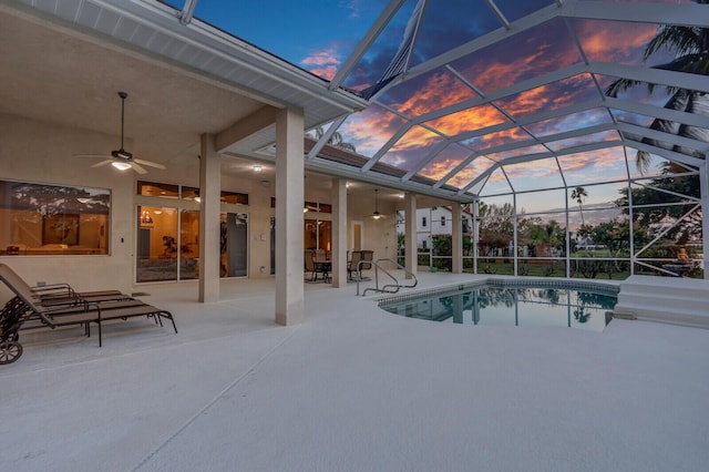 pool at dusk with ceiling fan, a patio, and glass enclosure