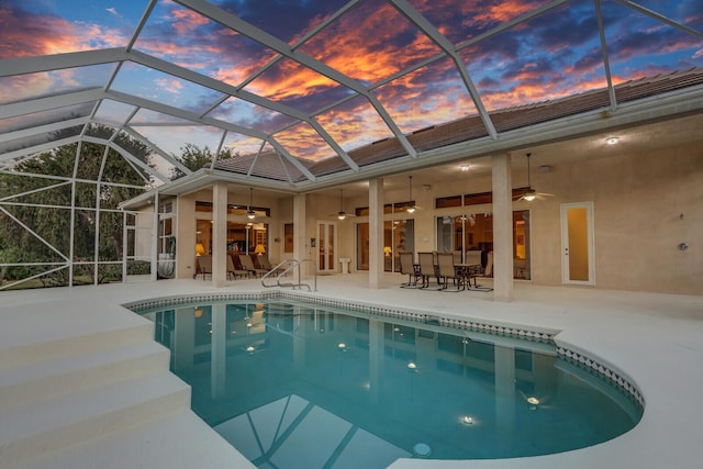 pool at dusk featuring a lanai, a patio area, and ceiling fan