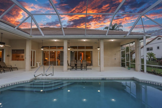 pool at dusk with a patio area, ceiling fan, and glass enclosure