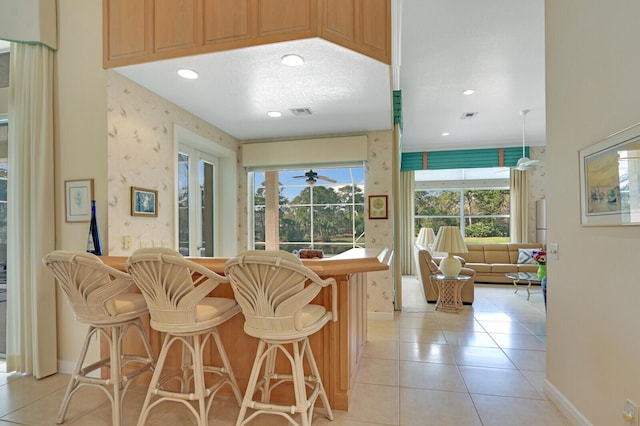 kitchen with ceiling fan, kitchen peninsula, a breakfast bar area, and light tile patterned floors