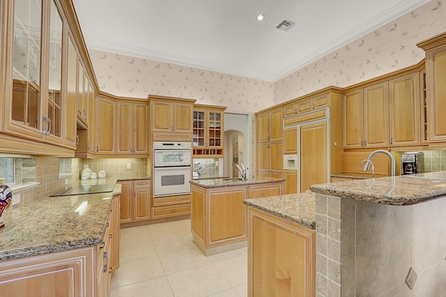 kitchen with white double oven, light stone counters, kitchen peninsula, paneled refrigerator, and a center island with sink