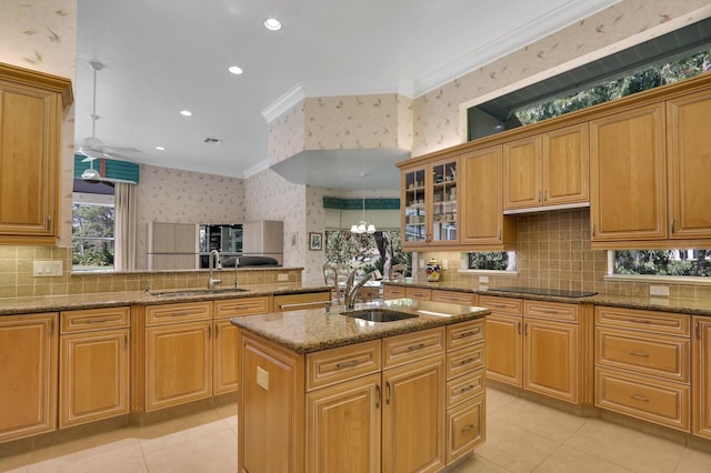 kitchen with sink, crown molding, light stone countertops, an island with sink, and black electric cooktop