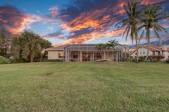 back house at dusk with a lanai and a lawn