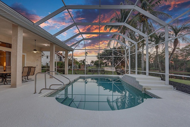 pool at dusk featuring a patio, ceiling fan, and glass enclosure