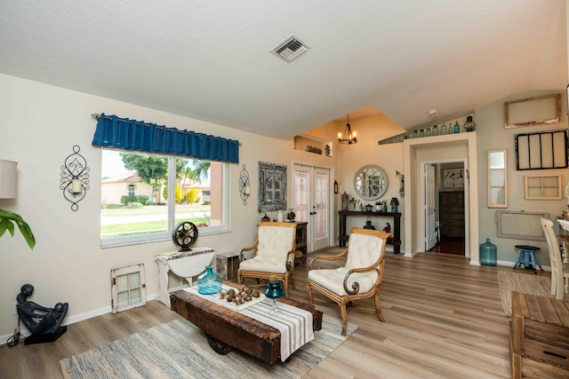 living area with hardwood / wood-style flooring, a notable chandelier, a textured ceiling, vaulted ceiling, and french doors