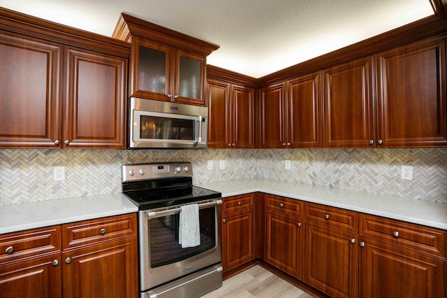 kitchen with stainless steel appliances, light wood-type flooring, and backsplash