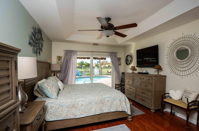 bedroom with dark hardwood / wood-style flooring, access to outside, ceiling fan, a raised ceiling, and a textured ceiling