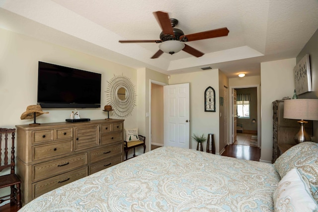 bedroom with ceiling fan, a tray ceiling, and a textured ceiling