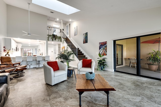 living room featuring ceiling fan, a towering ceiling, and a skylight