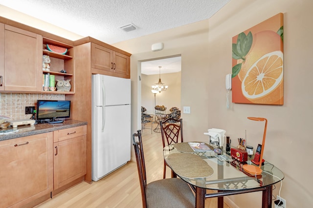 kitchen featuring a textured ceiling, hanging light fixtures, white refrigerator, light wood-type flooring, and decorative backsplash